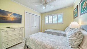A bedroom with two beds, a ceiling fan, a painting, and a window with blinds. - LaPlaya 107A-Soak up the sun or float in the warm Gulf waters. (Longboat Key)