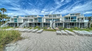 Een modern pand aan het strand met meerdere niveaus, buiten zitplaatsen en een heldere lucht.
