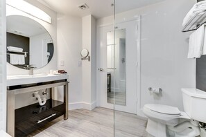 Features a glass-enclosed shower, large mirror, and vanity with sink and storage.