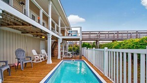 Ein Poolbereich mit Holzterrasse, weißen Geländern und Liegestühlen.