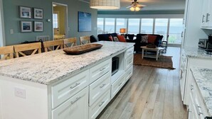 A spacious kitchen with a large island, white cabinetry, and a view to the outside. - Oceanfront 5BR beach house with pool in Holden Beach, perfect for 12 guests. (Holden Beach)