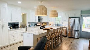 A modern kitchen with white cabinets, a stainless steel refrigerator, and a central island with bar stools. - Oceanfront 5BR beach house with pool in Holden Beach, perfect for 12 guests. (Holden Beach)
