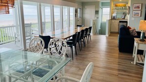A spacious dining area with a glass table and chairs, a kitchen area, and a view of the beach. - Oceanfront 5BR beach house with pool in Holden Beach, perfect for 12 guests. (Holden Beach)