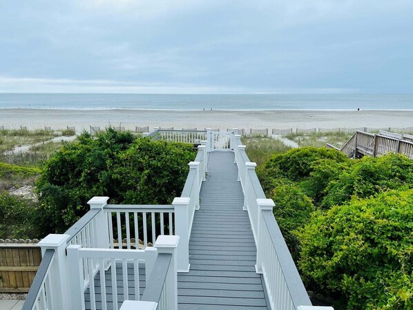 A wooden boardwalk leading to a beach with a fence and greenery.