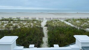 A beach view with a sandy path leading to the sea, surrounded by vegetation. - Oceanfront 5BR beach house with pool in Holden Beach, perfect for 12 guests. (Holden Beach)