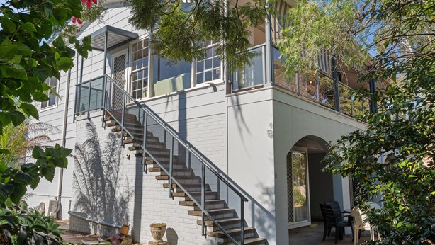 A two-story building with a staircase leading to the upper floor, a covered outdoor seating area, and a garden with potted plants.