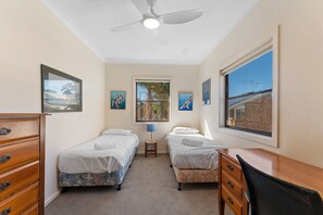 A bedroom with two single beds, a ceiling fan, a window with a view, and a desk with a chair.