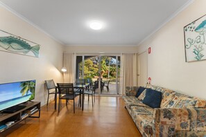A living room with a television, seating, and a view through a glass door to an outdoor area.