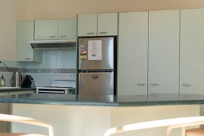 A kitchen with a stainless steel refrigerator, a stove, and a microwave. There are cabinets above the counter and a window above the stove.