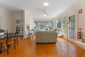 A spacious living area with a sofa, chairs, a dining table, and a ceiling fan.