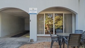 A covered outdoor seating area with a table and chairs, a sign for Port Stephens Holiday Rental, and a number '2' on the wall.