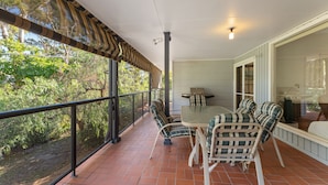 A covered patio with a table and chairs, a grill, and a view of the surrounding greenery.