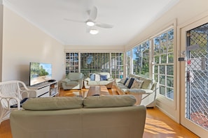 A spacious living room with a ceiling fan, large windows, and a television.