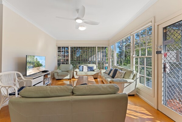 A spacious living room with a ceiling fan, large windows, and a television.