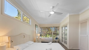 A bedroom with a bed, a bedside table, a lamp, a ceiling fan, and a window with a view of trees.