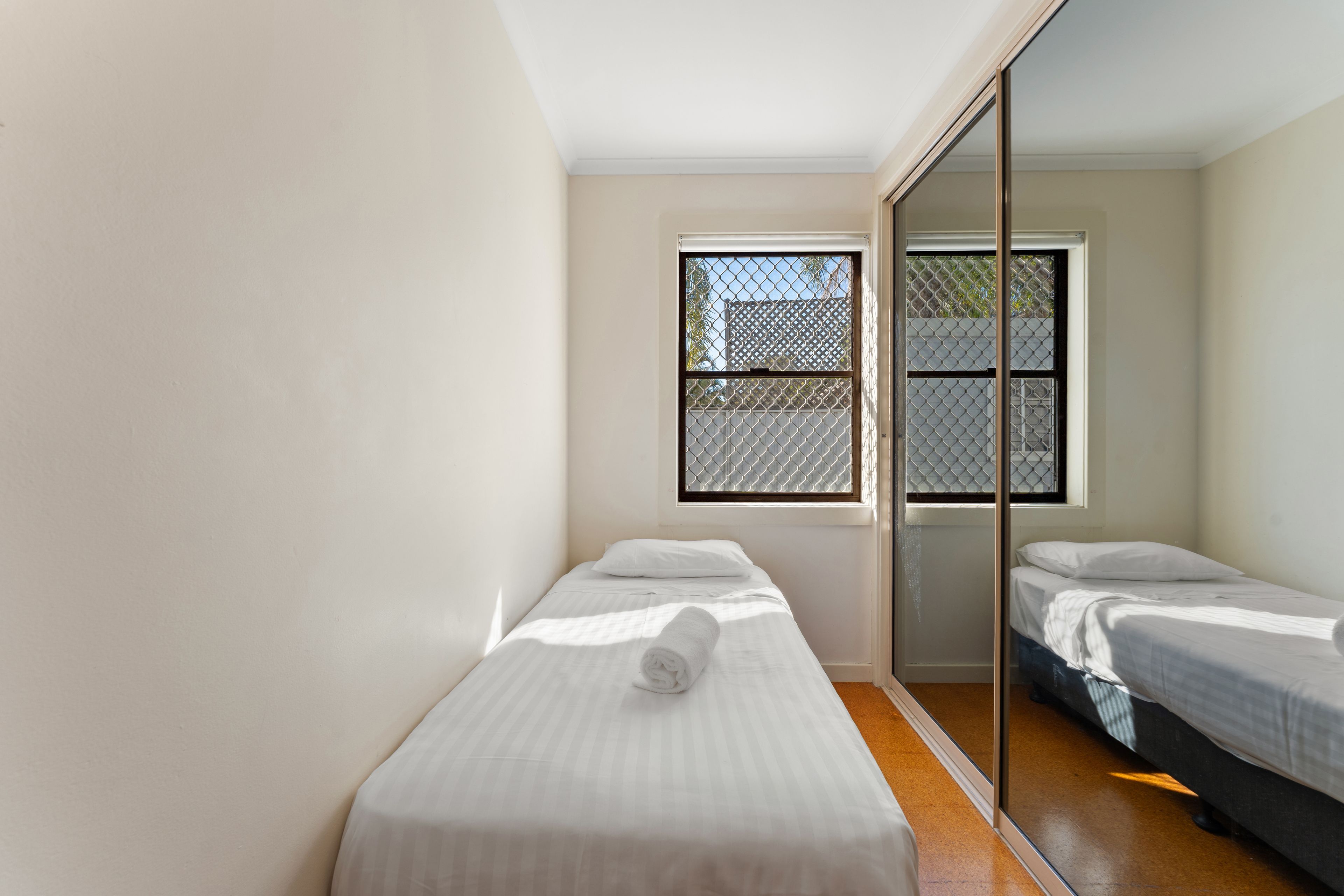 A room with two single beds, a sliding door, and a window with a metal screen.