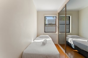 A room with two single beds, a sliding door, and a window with a metal screen.