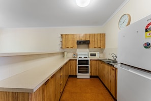 A compact kitchen with wooden cabinets, a microwave, a stove, and a refrigerator.