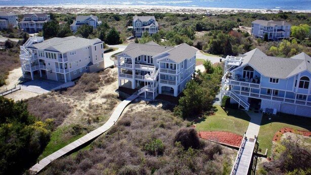 Uma propriedade costeira com várias casas grandes, vista para a praia e um calçadão.