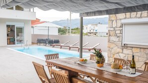 A poolside area with a wooden table, chairs, and a bottle of wine. - Villa Lele - Pool, Sea & Mountain View (Novigrad)