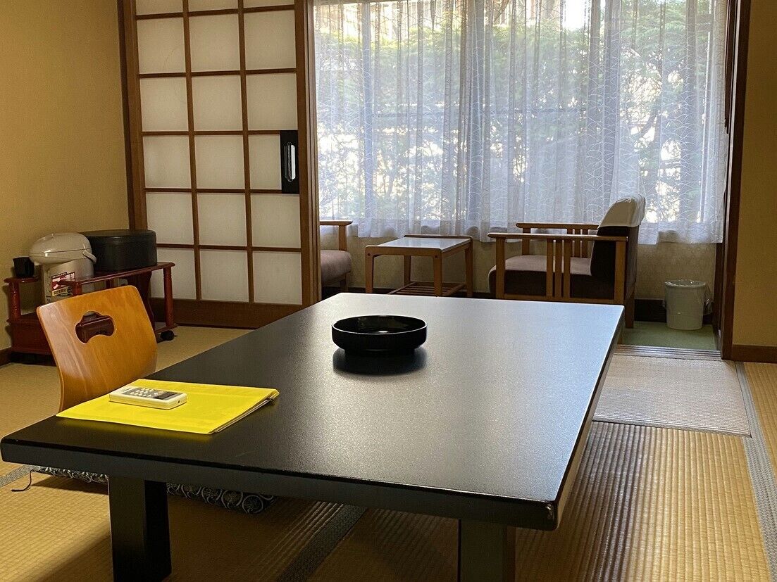 A traditional Japanese room with tatami flooring, a low table with a black tray, a yellow folder, and a wooden chair.
