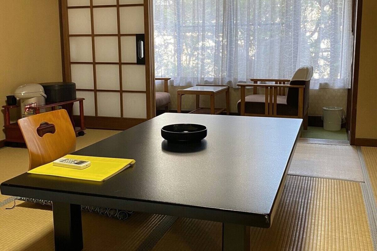 A traditional Japanese room with tatami flooring, a low table with a black tray, a yellow folder, and a wooden chair.