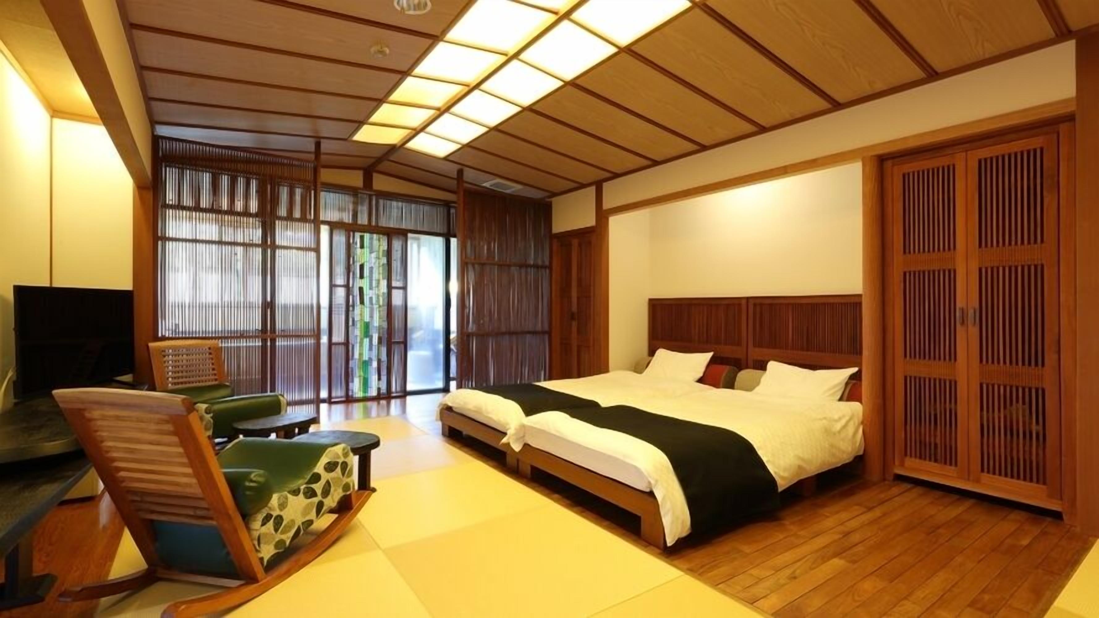 A traditional Japanese-style bedroom with tatami flooring, a low wooden bed, a desk with a chair, and sliding shoji doors.