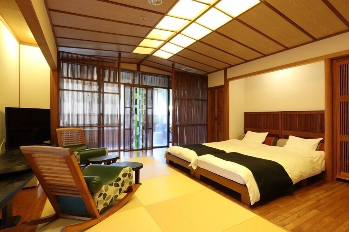 A traditional Japanese-style bedroom with tatami flooring, a low wooden bed, a desk with a chair, and sliding shoji doors.