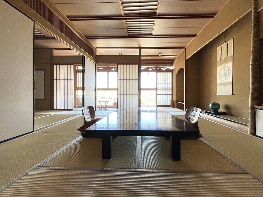 A traditional tatami room with a low table, tatami mats, sliding doors, and a view through the shoji screens.
