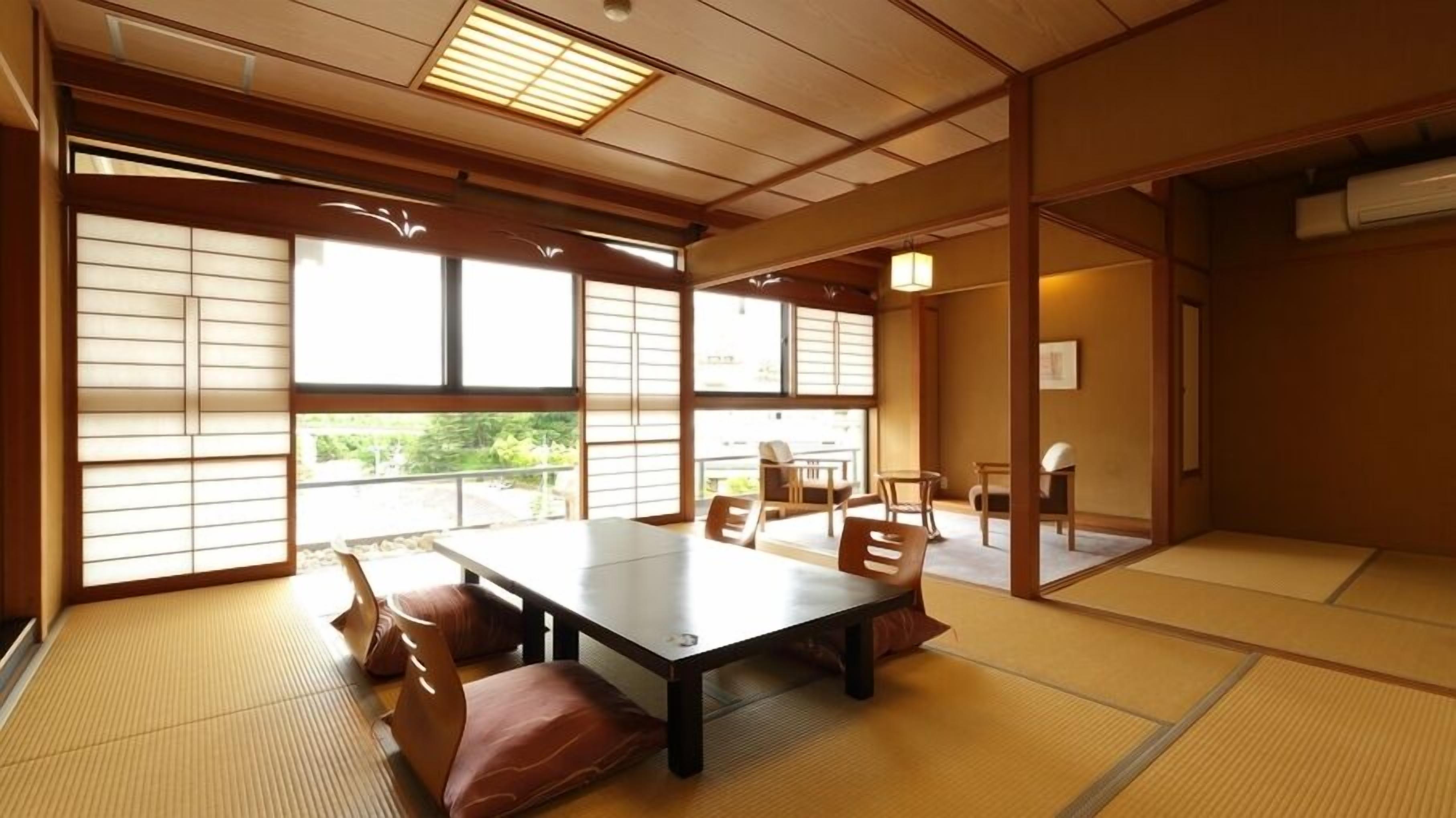 A tatami mat room with a low table and chairs, large windows, and a traditional Japanese interior.