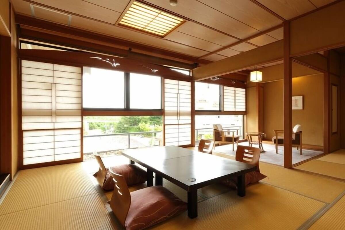 A tatami mat room with a low table and chairs, large windows, and a traditional Japanese interior.