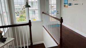 A staircase with a wooden handrail and white balusters, leading to a door with a window above it. - Compass Rose / 109 Sunshine: Spacious 4BR house in beach in Holden Beach, NC. (Holden Beach)