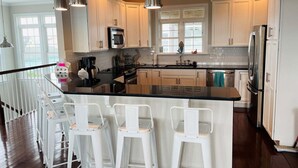A modern kitchen with white cabinets, a black countertop, and three white bar stools. - Compass Rose / 109 Sunshine: Spacious 4BR house in beach in Holden Beach, NC. (Holden Beach)