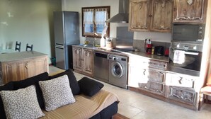 A compact kitchen with a washing machine, oven, and microwave. There is a dining table with chairs and a sofa with cushions. - Wonderful house at the heart of Provence 1km to beach with terrace and parking (Fos-Sur-Mer)