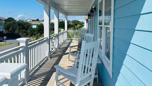 A covered porch with white railings and chairs, a clear view of the surrounding neighborhood, and a blue building facade. - Experience bliss at Blue Sunset in Holden Beach, NC! Sleeps 8. (Holden Beach)