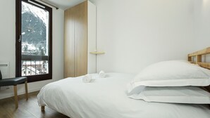 Een slaapkamer met een houten bed, een bankje, een raam met uitzicht op bergen, en een houten garderobe.