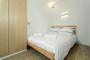 A bedroom with a wooden bed, white linens, and a wooden wardrobe.