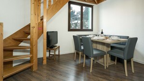Een eetruimte met een houten trap, een televisie en een tafel gedekt voor vier personen.