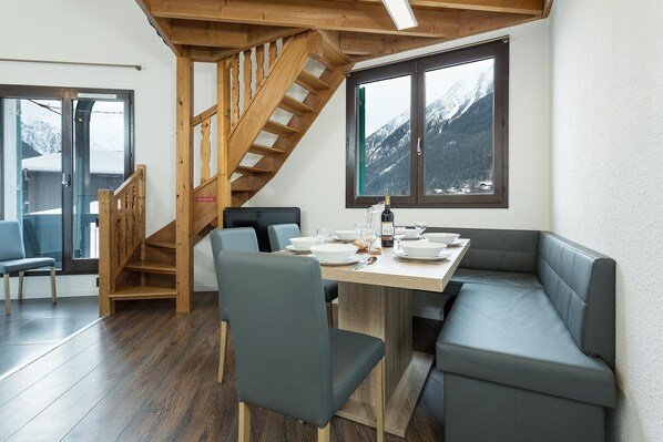 A dining area with a wooden staircase, a table set for four, and a view of snow-capped mountains through a window.