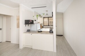 A compact kitchen with white cabinetry, a built-in microwave, and a kettle on the counter.