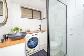 Een kleine keuken met een wasmachine, een spoelbak en een grote kom op het aanrecht.