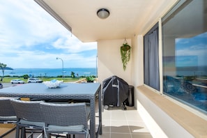 Een balkon met uitzicht op zee, een tafel met stoelen en een grillhoes.