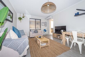 A modern living room with a sofa, coffee table, TV, and dining area.