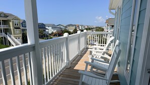 A wooden deck with white railings and rocking chairs, overlooking a residential area with houses.