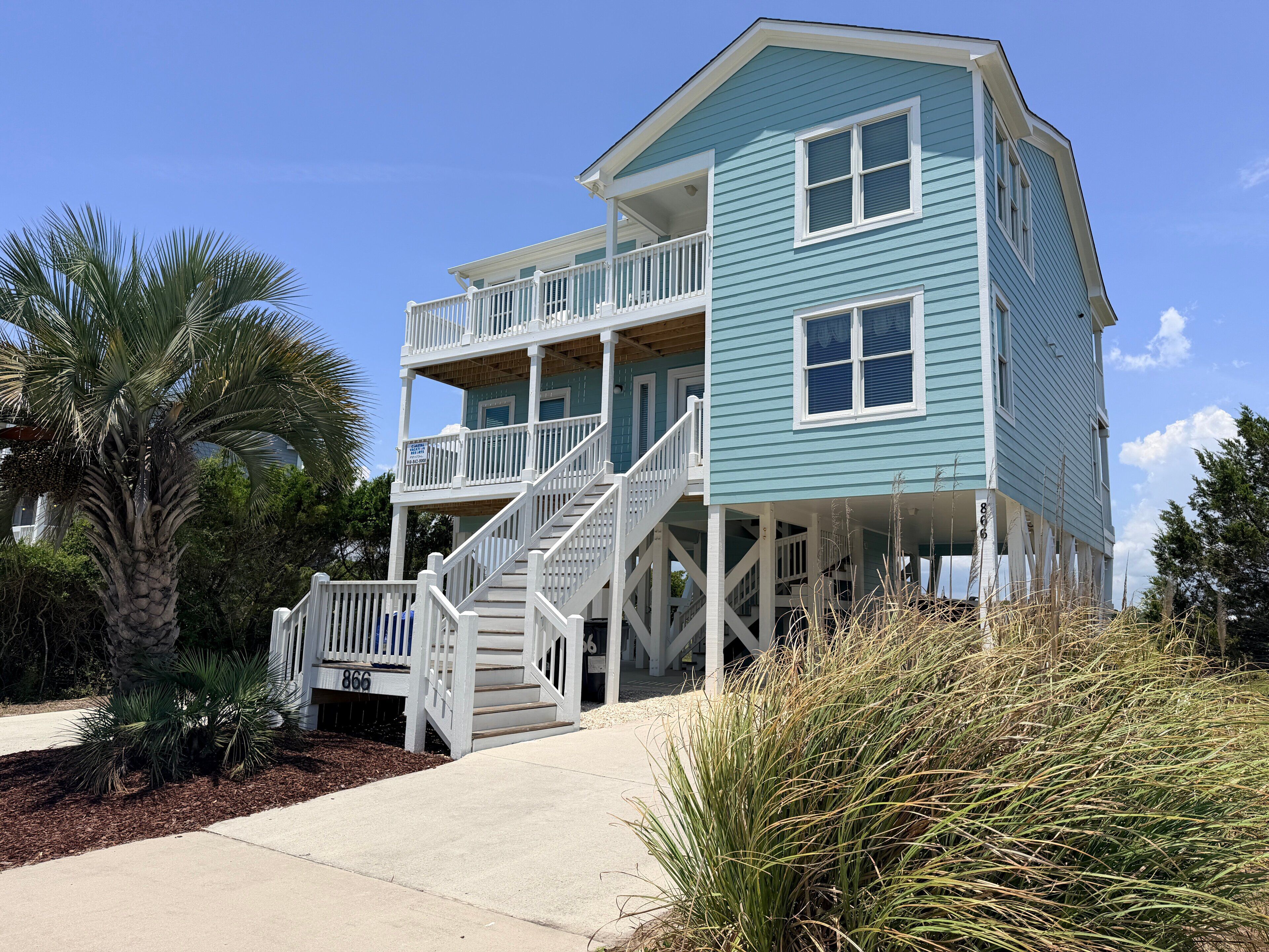 A multi-story beachfront house with a balcony, a staircase, and a number 866 sign.