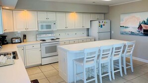 A kitchen with white cabinets, a microwave, a stove, a refrigerator, and a dining area with chairs.