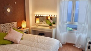 Ein Schlafzimmer mit Bett, Nachttisch, Lampe, Schminktisch mit Spiegel und einem Fenster mit Vorhängen.