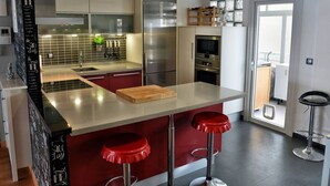 Eine moderne Küche mit Kochinsel, roten Barhocker, Edelstahlgeräten und einer gefliesten Spritzschutzwand.