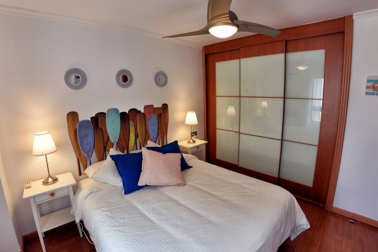 Un dormitorio con cama, dos mesitas de noche con lámparas, ventilador de techo y armario con puerta corredera de vidrio.