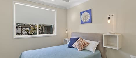 A bedroom with a bed, a window, a ceiling fan, a wall-mounted light, and a decorative wall piece.